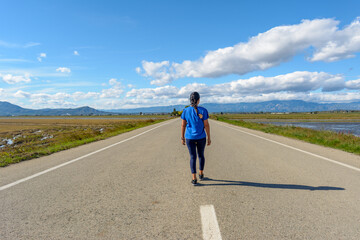 A person is walking down an open road surrounded by nature