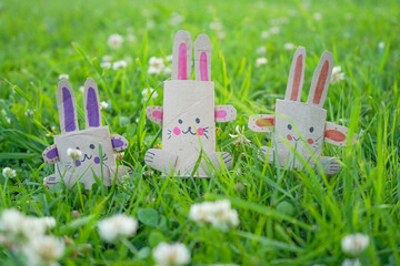 Kids craft bunnies out of recycling toilet paper roll on the green grass, zero waste concept.