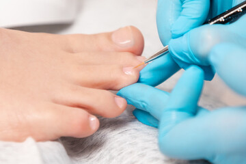 A pedicure master in medical gloves takes care of beautiful female toenails. Close-up. The concept of chiropody and podology - obrazy, fototapety, plakaty