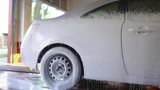 Auto detailer blankets car in luxurious foam, creating a captivating scene. The vehicle, immersed in suds, showcasing thorough cleansing artistry.