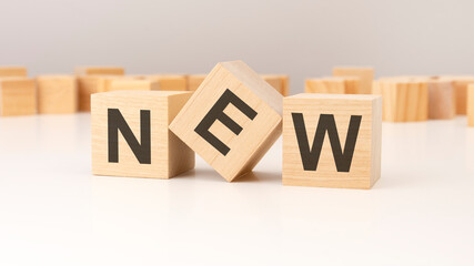 wooden cubes standing on a white table against a gray wall, inscribed with 'NEW'