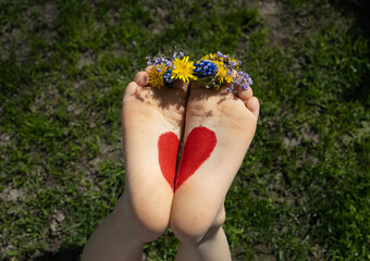 flowers between toes and a red heart drawn on bare feet of a child lying on the grass on a sunny day. Cheerful childhood, childish love. positive atmosphere, tender feelings. mother's day, earth day