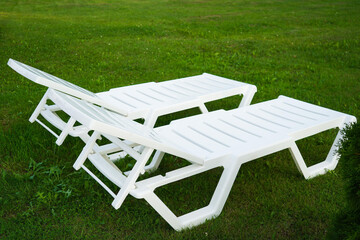 Empty white plastic chair or chaise longue, on the green grass of a fresh lawn. Recreation and...
