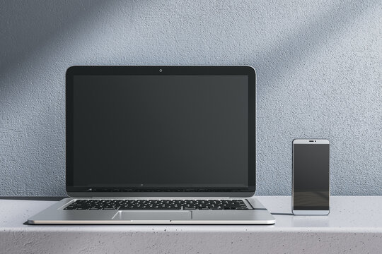 Close up of empty laptop and smartphone on gray desk. Concrete wall background. Device presentation and online education concept. Mock up, 3D Rendering.