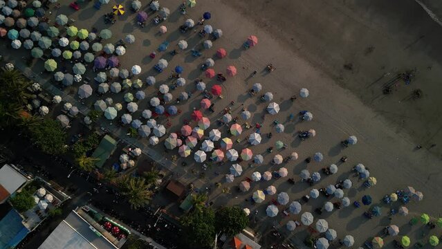 Aerial view of Beautiful sunset on the double six beach with Hotel, resort, cafe buildings, beach umbrella and calm ocean wave in Bali. Tourists are surfing, swimming and walking along the beach.