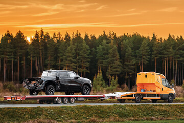 A tow truck evacuates a broken pick-up truck on a flatbed trailer from the interstate highway,...