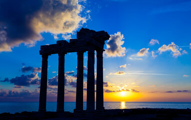 Ancient ruins at sunset over the sea, reflecting in the water.