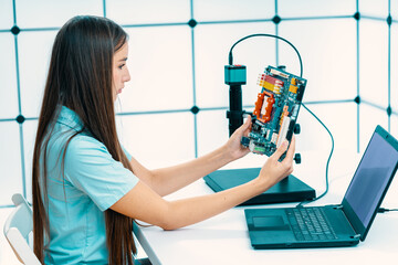 young woman in an electronics laboratory testing a printed circuit board using a microscope