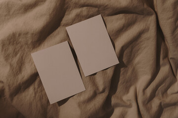 Paper sheets with blank copy space on crumpled tan beige bed blanket with sunlight shadows. Styled...