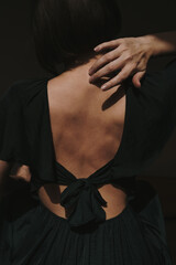Back view of pretty woman in black dress with naked back and tan skin. Aesthetic elegant chic boho...