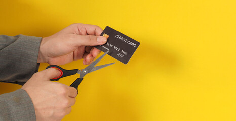 Hand is hold black credit card and scissors on yellow background. Man arm wear a grey suit