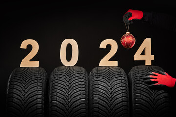 2024 happy new year, winter care tires and hands of a man with christmas tree ball on black background.