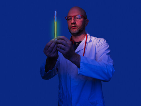 Doctor working in a lab concept. Male healthcare specialist holding glass flask with green glowing liquid in a blue lab room. Development of new vaccine or medicine product for mass consumption.