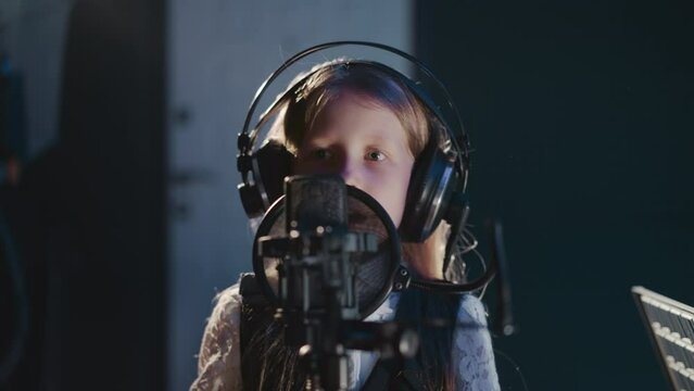 Vocalist moves hand while singing closeup. Child catches beat while recording song in recording studio. Skilled kid wearing headphones in audio studio