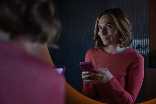 Woman looking at reflection in mirror holding a smartphone getting ready to go out