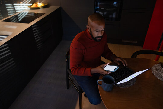 Man working on laptop late at night at home in kitchen