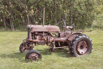 rusted antique tractor parked in a lush green hayfield at a farm museum in Iceland with blurred trees in the background
