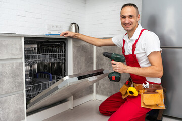 Young Repairman Fixing Dishwasher With Electric Drill