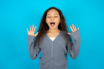 Emotive Beautiful teen girl wearing blue jacket over blue background laughs loudly, hears funny joke or story, raises palms with satisfaction,