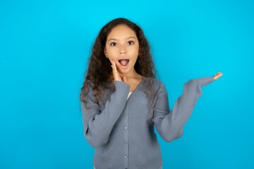 Crazy Beautiful teen girl wearing blue jacket over blue background advising discount prices hold...