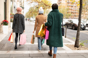 Group of female friends with colorful shopping bags strolling through city streets, enjoying the festive season's sales and winter fashion. - obrazy, fototapety, plakaty