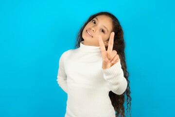 Young beautiful teen girl wearing white turtleneck over blue background directs fingers at camera selects someone. I recommend you. Best choice