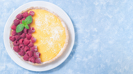 Lemon tart, garnished with fresh raspberry, on white plate, horizontal top view, copy space