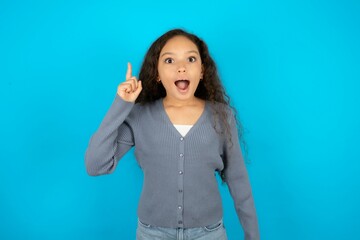 Beautiful teen girl wearing blue jacket over blue background pointing finger up and looking...