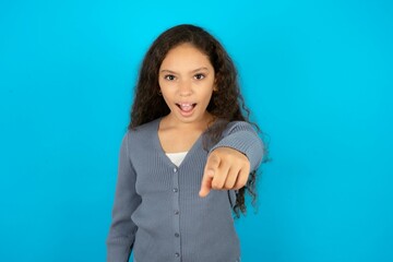 Beautiful teen girl wearing blue jacket over blue background pointing displeased and frustrated to...
