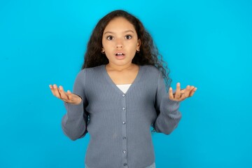 Frustrated Beautiful teen girl wearing blue jacket over blue background feels puzzled and hesitant,...
