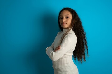 Portrait of Young beautiful teen girl wearing white turtleneck over blue background standing with folded arms and smiling