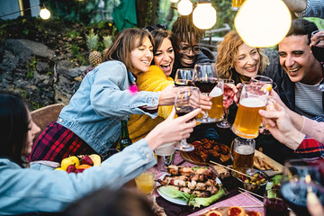 Joyful group of diverse friends toasting with wine and beer, enjoying a barbecue party outdoors,...