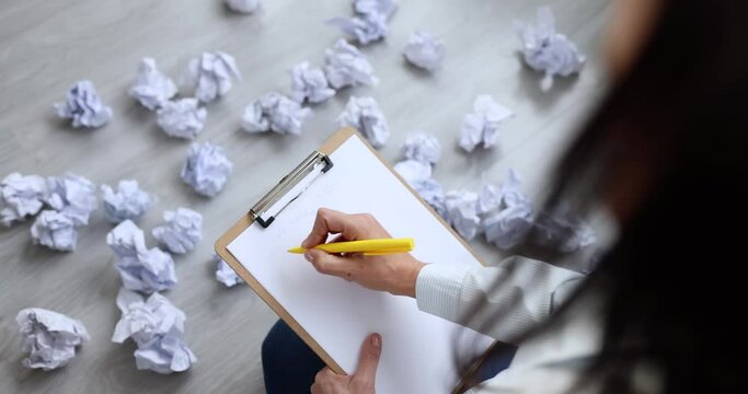 Woman writing business plan near documents crumpled and scattered on floor 4k movie slow motion. Difficulty planning work strategies concept