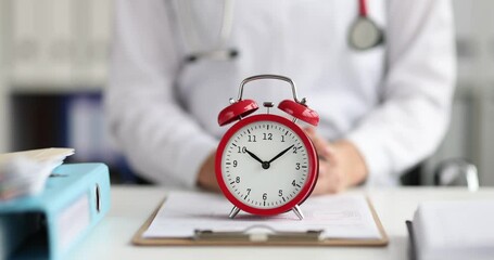 Red alarm clock standing on doctor table in clinic 4k movie slow motion. Clinic working hours concept