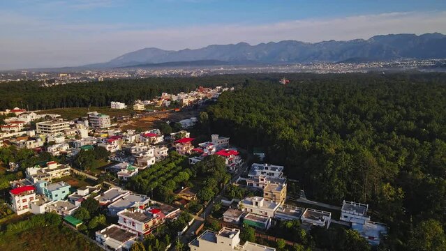 An aerial view of Dehradun, an Indian city during sunrise or sunset, with cloudy weather and rows of residential houses surrounded with greenery. The Himalayan city is surrounded by rainforest.