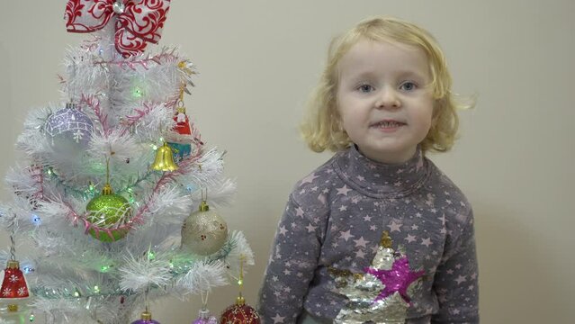 a little girl carols by the Christmas tree, funny cheerful child caroling for Christmas at home
