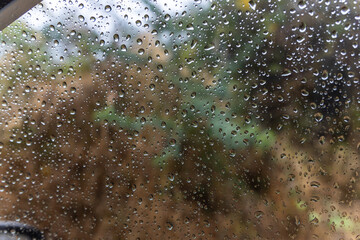 rain drops sliding at car window glass at rainy day from flat angle