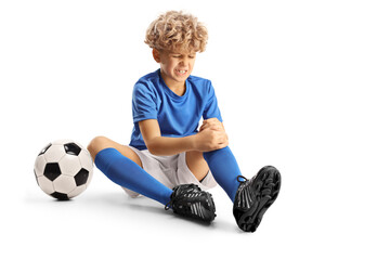 Boy with a football sitting on the ground and holding his injured knee