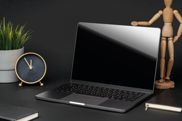 Open laptop with wooden mannequin on table against black background