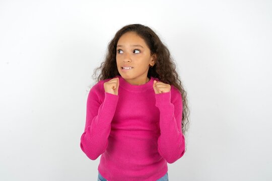 Young beautiful teen girl clenches fists and awaits for something nice happened looks away bites lips and waits announcement of results