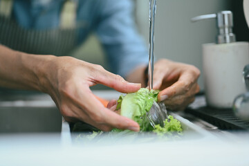 Closeup hands washing vegetables in the kitchen sink and preparing healthy food.