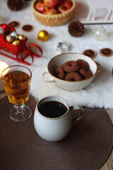 Cup of tea or coffee, glass of wine or juice, bowl of cookies, organic pomegranate, fluffy blanket, pine cones, various Christmas decorations and lit candles on the table. Christmas hygge concept.