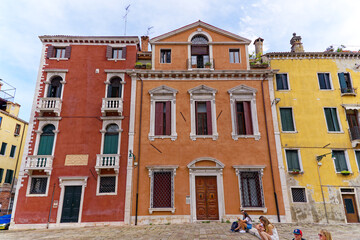 Fototapeta na wymiar Looking up colorful weathered facades of medieval houses with relaxing sitting tourists at City of Venice on a cloudy summer day. Photo taken August 6th, 2023, Venice, Italy.