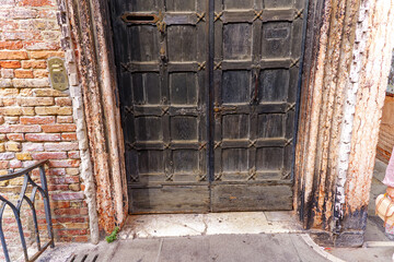 Close-up wooden weathered door of historic building at Italian City of Venice on a blue cloudy summer day. Photo taken August 6th, 2023, Venice, Italy.