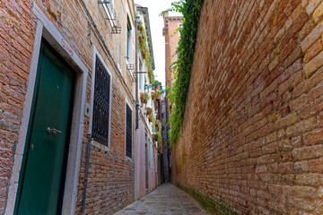 Diminishing perspective of narrow alley at the old town of Venice with facades of historic houses on a sunny summer day. Photo taken August 6th, 2023, Venice, Italy.
