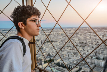 Paris, France, July 1, 2022. A young man is captivated by the breathtaking view of the city from above: from the terrace of the Eiffel Tower the sunset is a unique spectacle.