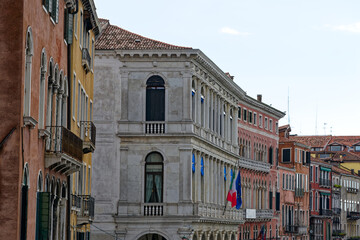 Looking up colorful facades of medieval houses with flags at Italian City of Venice on a cloudy summer day. Photo taken August 6th, 2023, Venice, Italy.