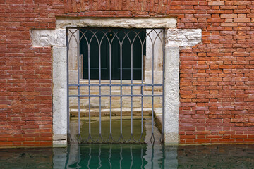 Old town of Venice with close up gate with grid and canal on a blue cloudy summer day. Photo taken August 6th, 2023, Venice, Italy.