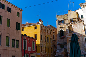 Looking up alley with colorful weathered facades of medieval houses at City of Venice on a cloudy summer day. Photo taken August 6th, 2023, Venice, Italy.