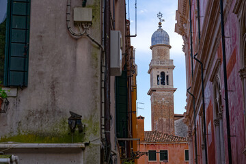 Looking up narrow alley with church tower and colorful weathered facades of medieval houses at City of Venice on a cloudy summer day. Photo taken August 6th, 2023, Venice, Italy.